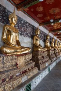 A row of golden Buddhas seated in Wat Suthat, Bangkok, showcasing intricate details and serene expressions. Must-Visit Temples in Bangkok.