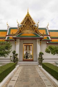 Wat Suthat in Bangkok features a striking white building topped with a gleaming gold roof against a bright sky. Must-Visit Temples in Bangkok.