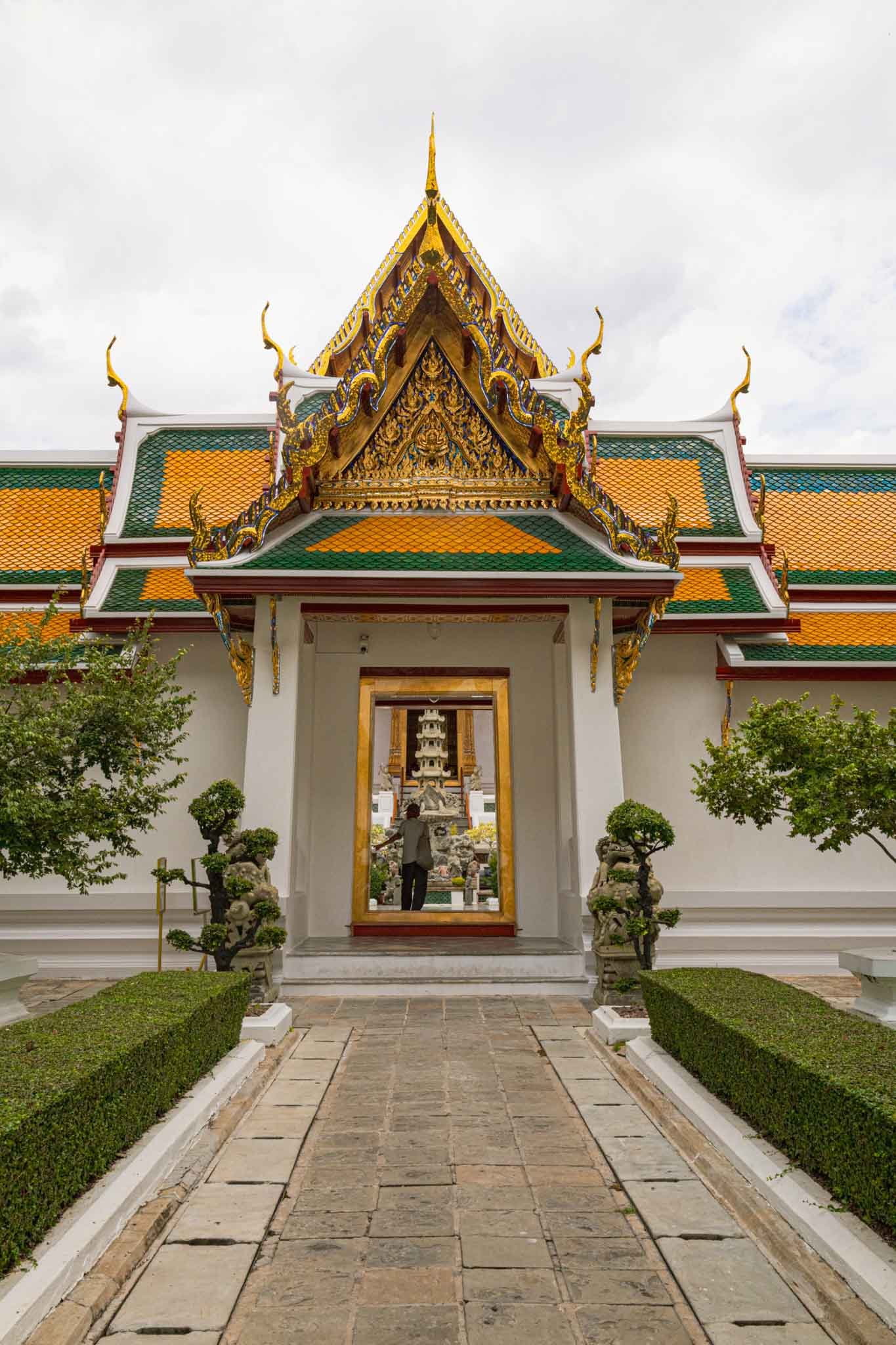 Wat Suthat in Bangkok, Thailand - Yati Travel Wat Suthat in Bangkok features a striking white building topped with a gleaming gold roof against a bright sky. Must-Visit Temples in Bangkok.