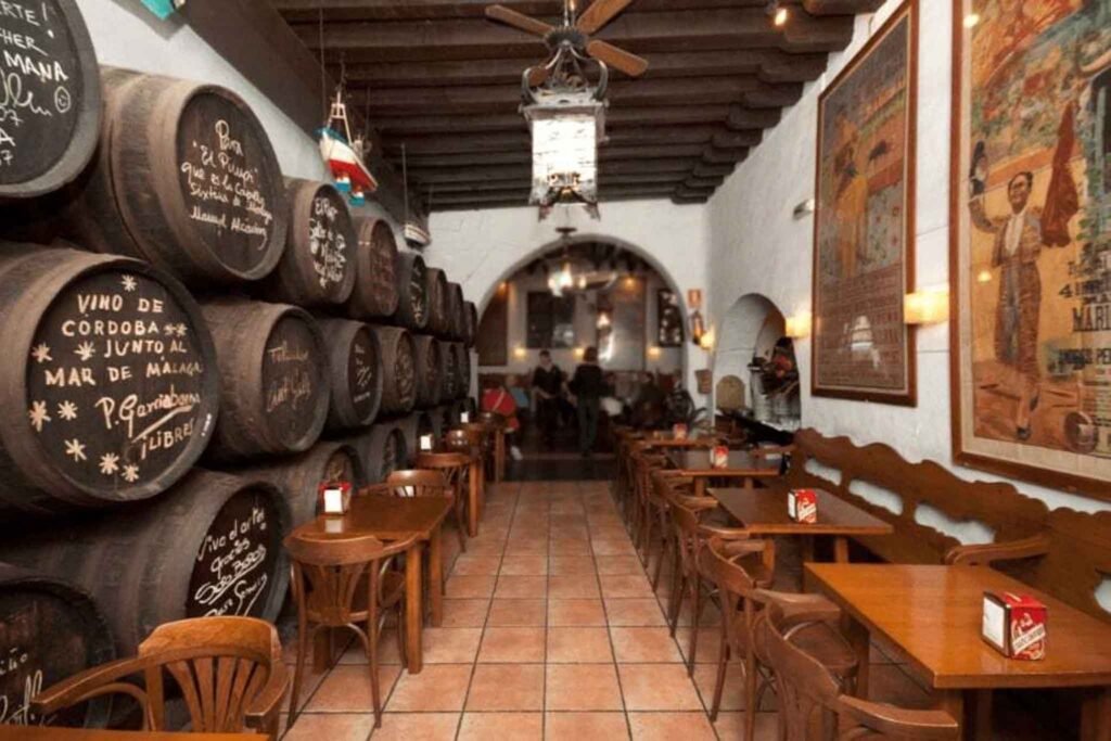 Cozy restaurant Bodega El Pimpi in Málaga, featuring wooden tables, chairs, and barrels of wine for a rustic atmosphere. Best Places to Eat in Málaga.