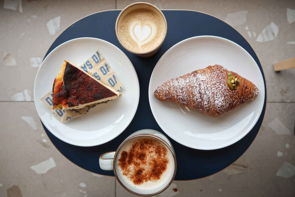 Two plates with cheesecake and a croissant, alongside a cup of coffee at Salvo Bakehouse in Amsterdam. Best Bakeries in Amsterdam.