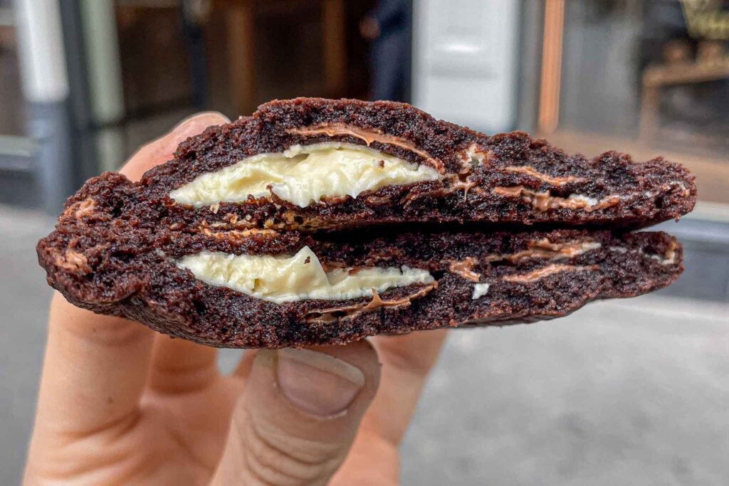 A person proudly holds a chocolate cookie with cream filling from Van Stapele Koekmakerij, showcasing its deliciousness. Best Bakeries in Amsterdam.