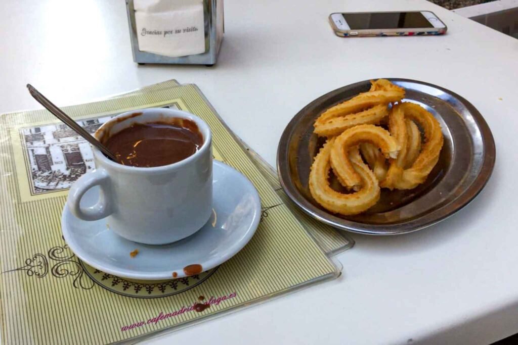 A cup of coffee and churros on a table at Café Madrid in Málaga, Spain, inviting a cozy snack experience. Best Places to Eat in Málaga.