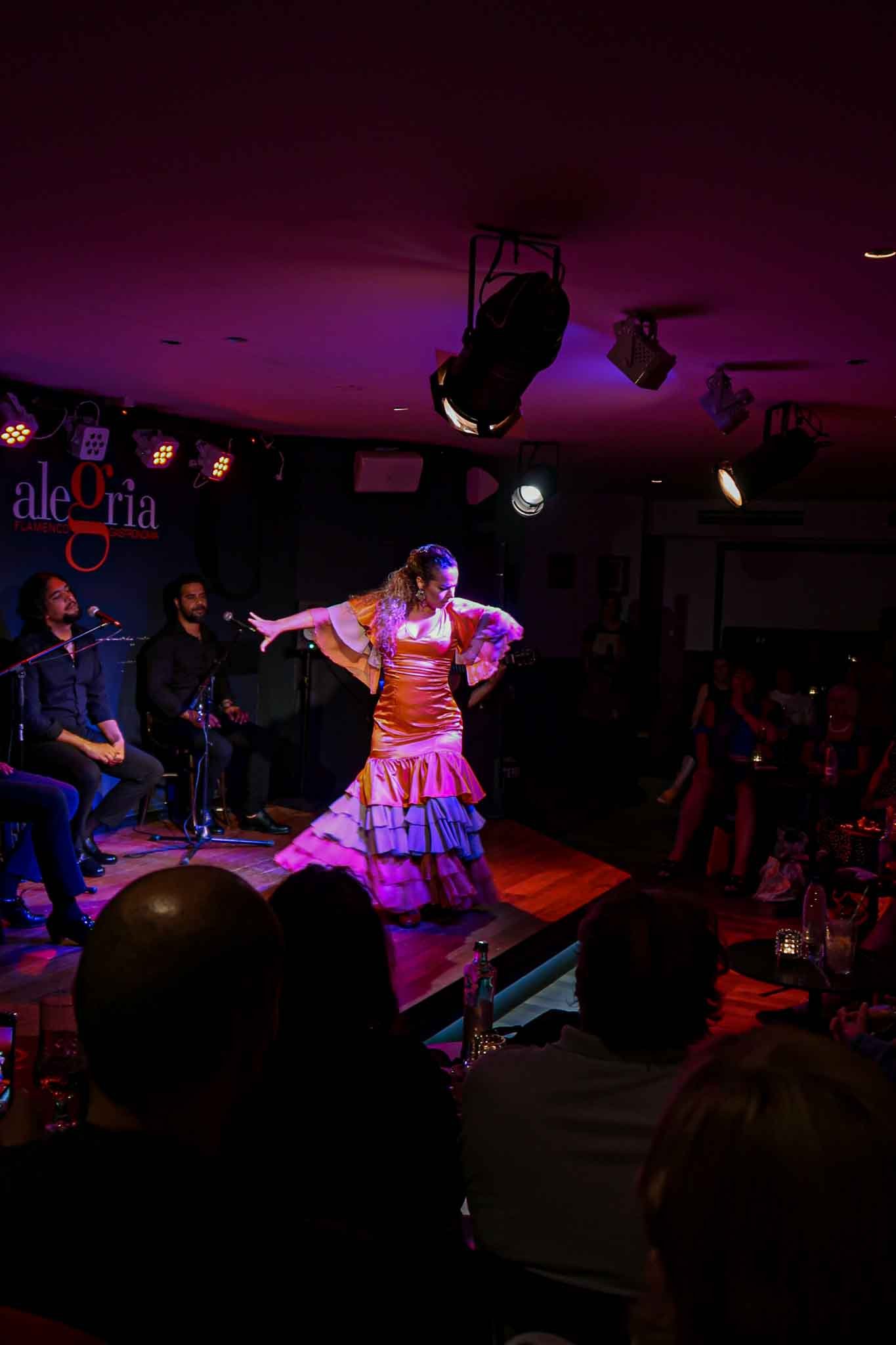 Flamenco Show at Alegría Flamenco y Gastronomía in Málaga, Spain V1 - Yati Travel A woman in a vibrant flamenco dress performs passionately on stage at Alegría Flamenco y Gastronomía in Málaga, Spain. Best Things to Do in Málaga.