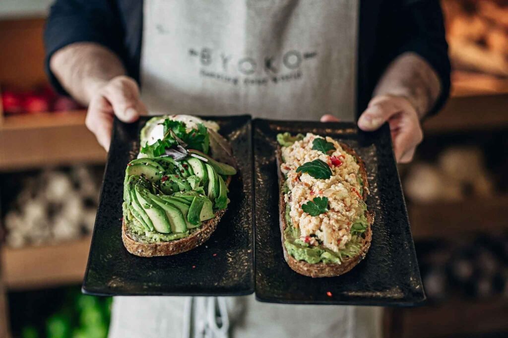 A man holds two plates of different dishes at BYOKO Merced in Málaga, Spain, showcasing a variety of food options. Best Places to Eat in Málaga.