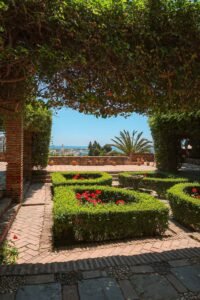 Lush garden inside Alcazaba, Málaga, with a stunning view of the ocean in the background. Best Things to Do in Málaga.