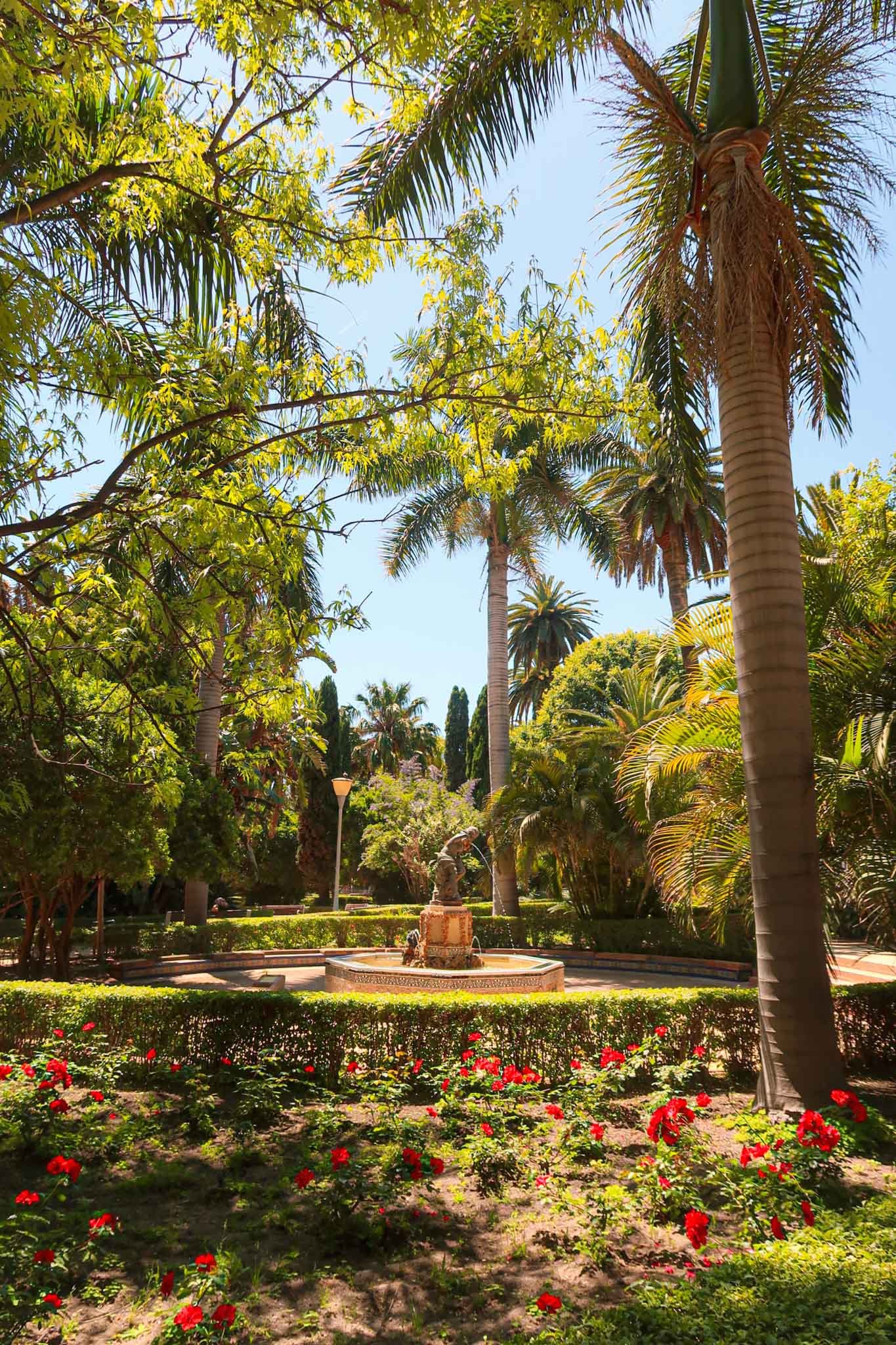 Inside Parque de Málaga V1 - Yati Travel A scenic view of Parque de Málaga featuring a fountain surrounded by lush palm trees. Best Things to Do in Málaga.