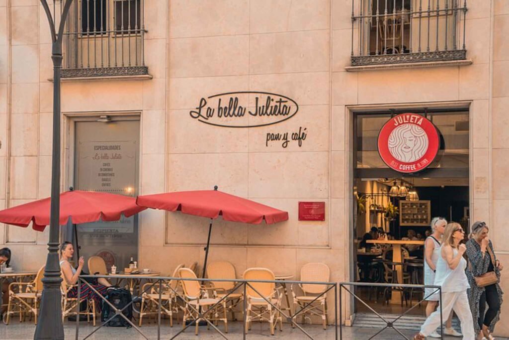 A group of people strolls past Julieta Coffee, a charming cafe in Málaga, Spain, enjoying the vibrant atmosphere. Best Places to Eat in Málaga.