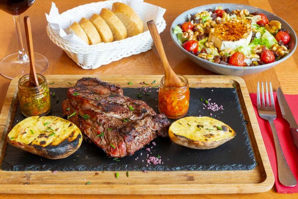 A delicious steak, fresh salad, and bread arranged on a cutting board at Pampa Grill in Málaga, Spain. Best Places to Eat in Málaga.