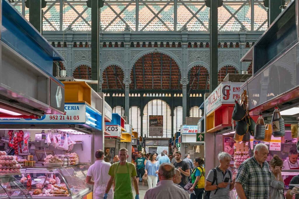 People stroll through Mercado de Atarazanas in Málaga, Spain, surrounded by vibrant stalls of fresh food and local delicacies. Best Places to Eat in Málaga.