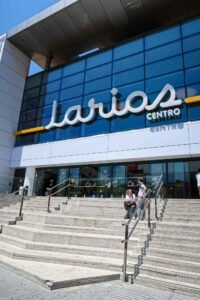 A man and woman sit on the steps outside Centro Comercial Larios Centro in Málaga, Spain, enjoying the sunny day. Best Things to Do in Málaga.