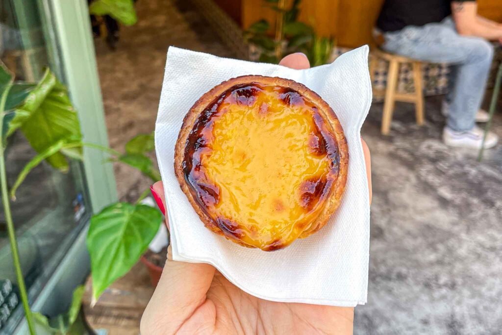 A person holding a Pastel de Nata pastry at Mr Nata in Amsterdam, showcasing its flaky crust and creamy filling. Best Bakeries in Amsterdam.