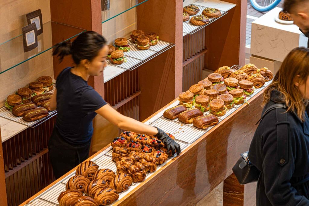 A woman stands at a counter displaying a variety of delicious pastries at Pantopia in Amsterdam. Best Bakeries in Amsterdam.