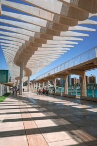 A walkway beneath a large, modern structure at Palmeral de Las Sorpresas in Málaga, Spain, surrounded by palm trees. Best Things to Do in Málaga.